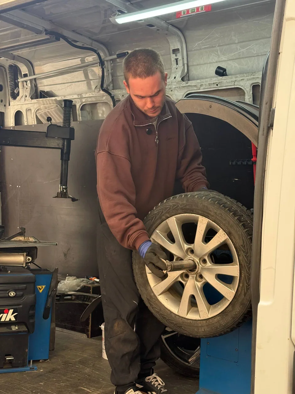 Мастер закрепляет колесо на балансировочном станке внутри фургона